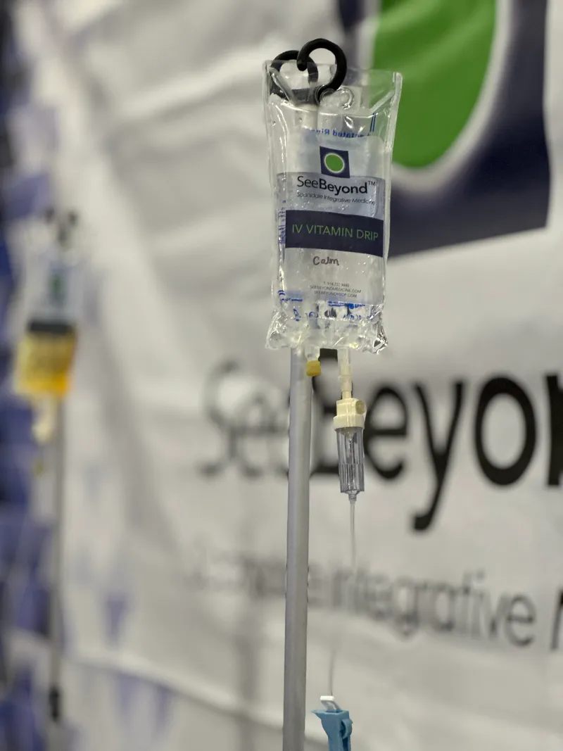SeeBeyond IV vitamin drip bag labeled Calm hanging on an IV pole in front of a SeeBeyond banner