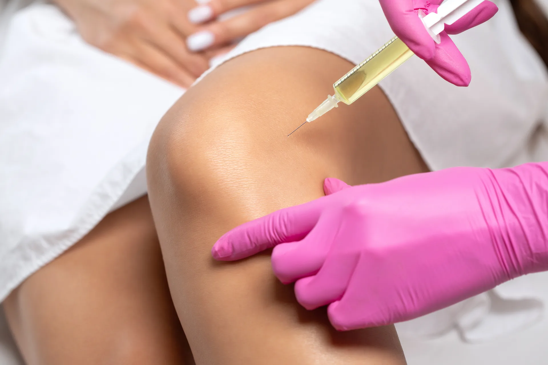 Gloved clinician injects yellow fluid from a syringe into a patient's knee