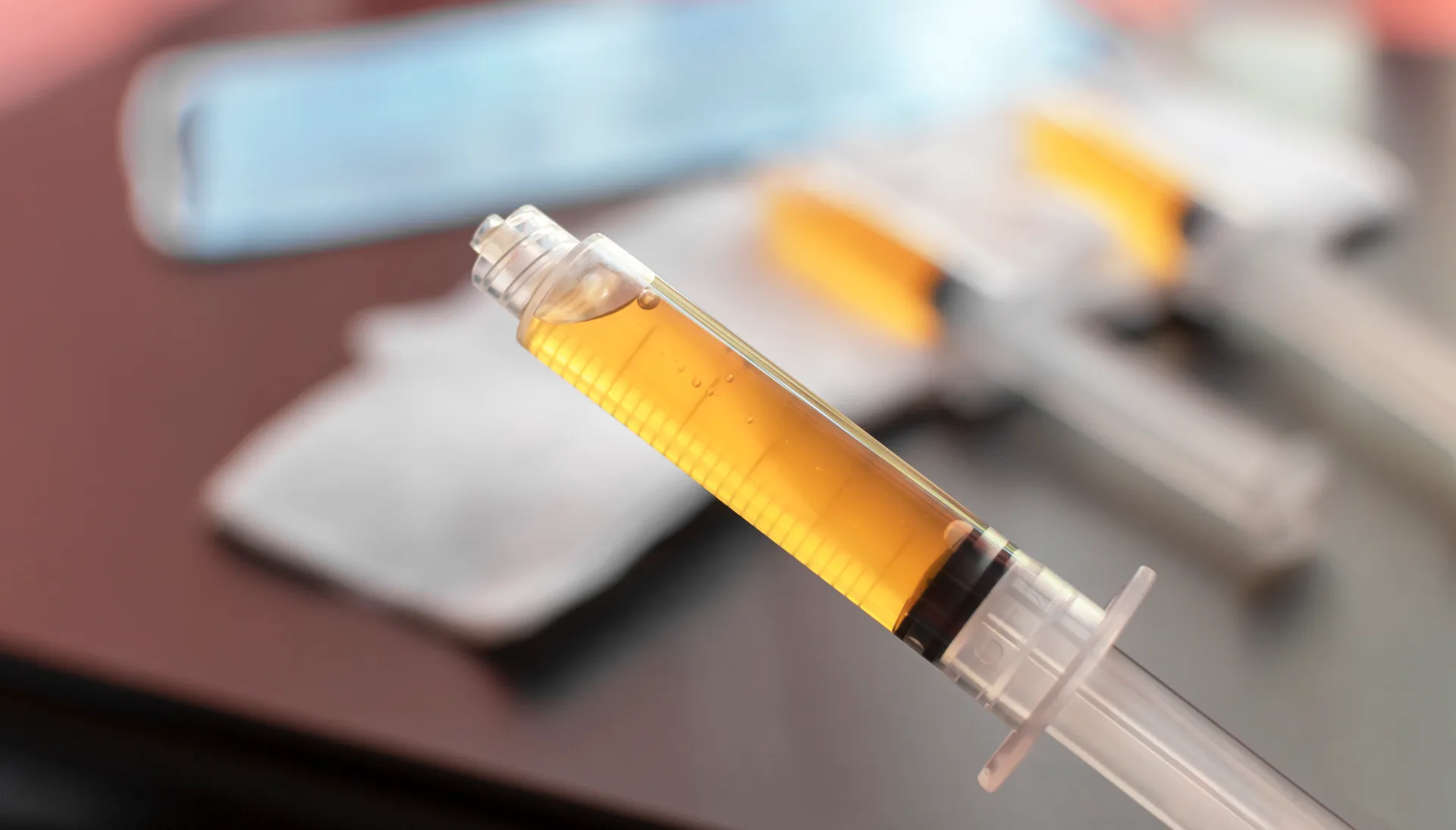 Syringe filled with amber liquid, with more syringes blurred in the background