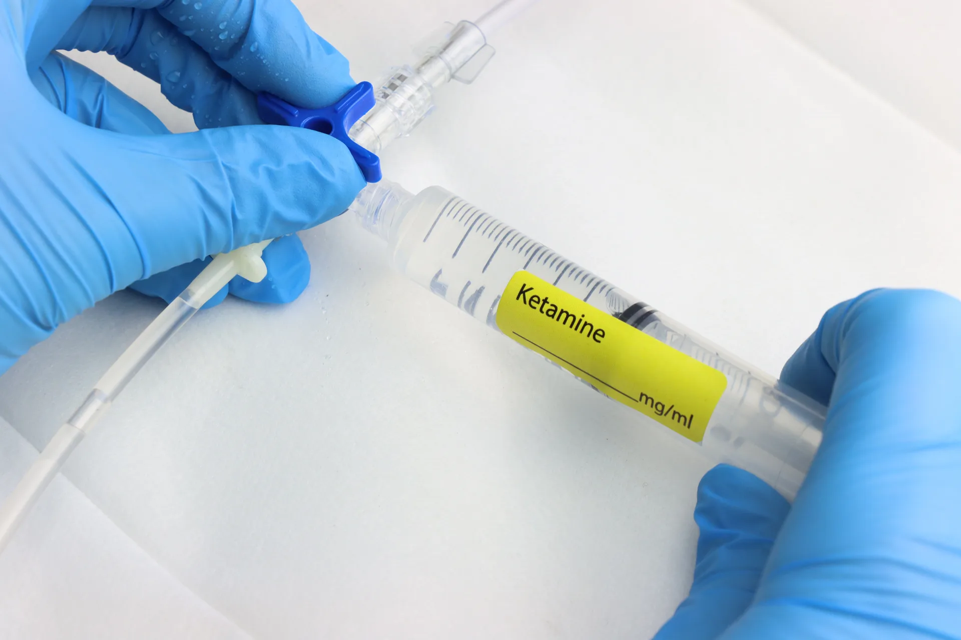 Gloved hands connecting a syringe labeled ketamine to an IV line