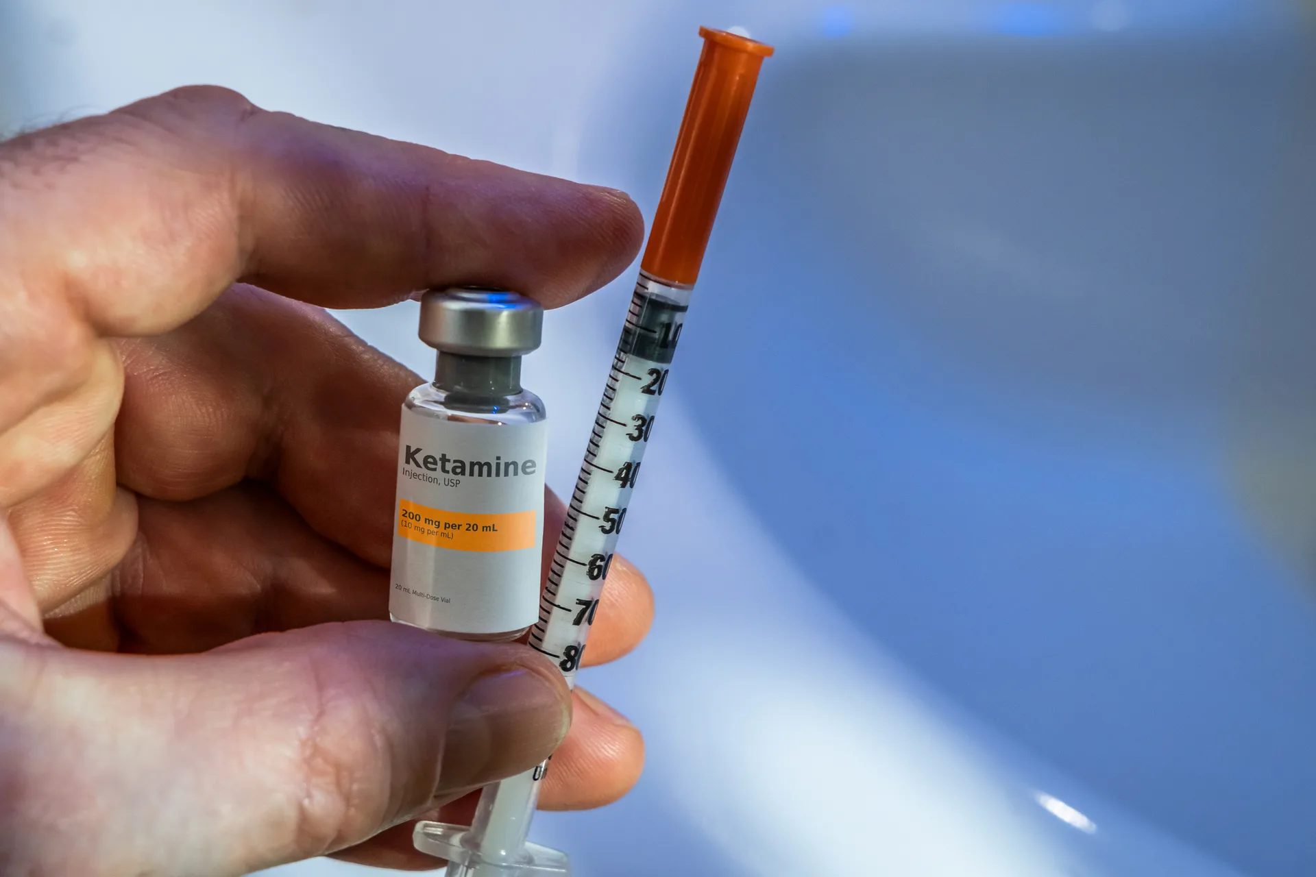 Hand holding a small ketamine vial next to an insulin syringe