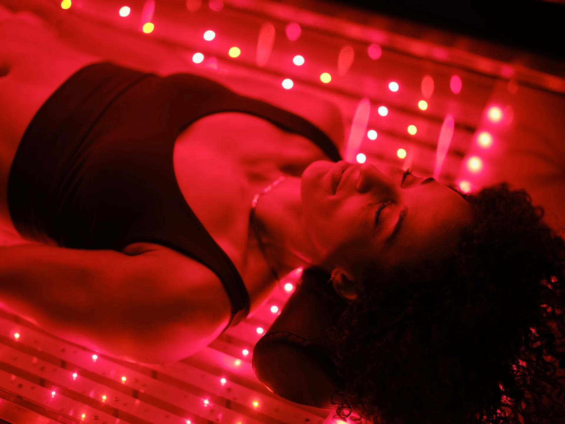 Woman with eyes closed lies on a bed of glowing red LED lights