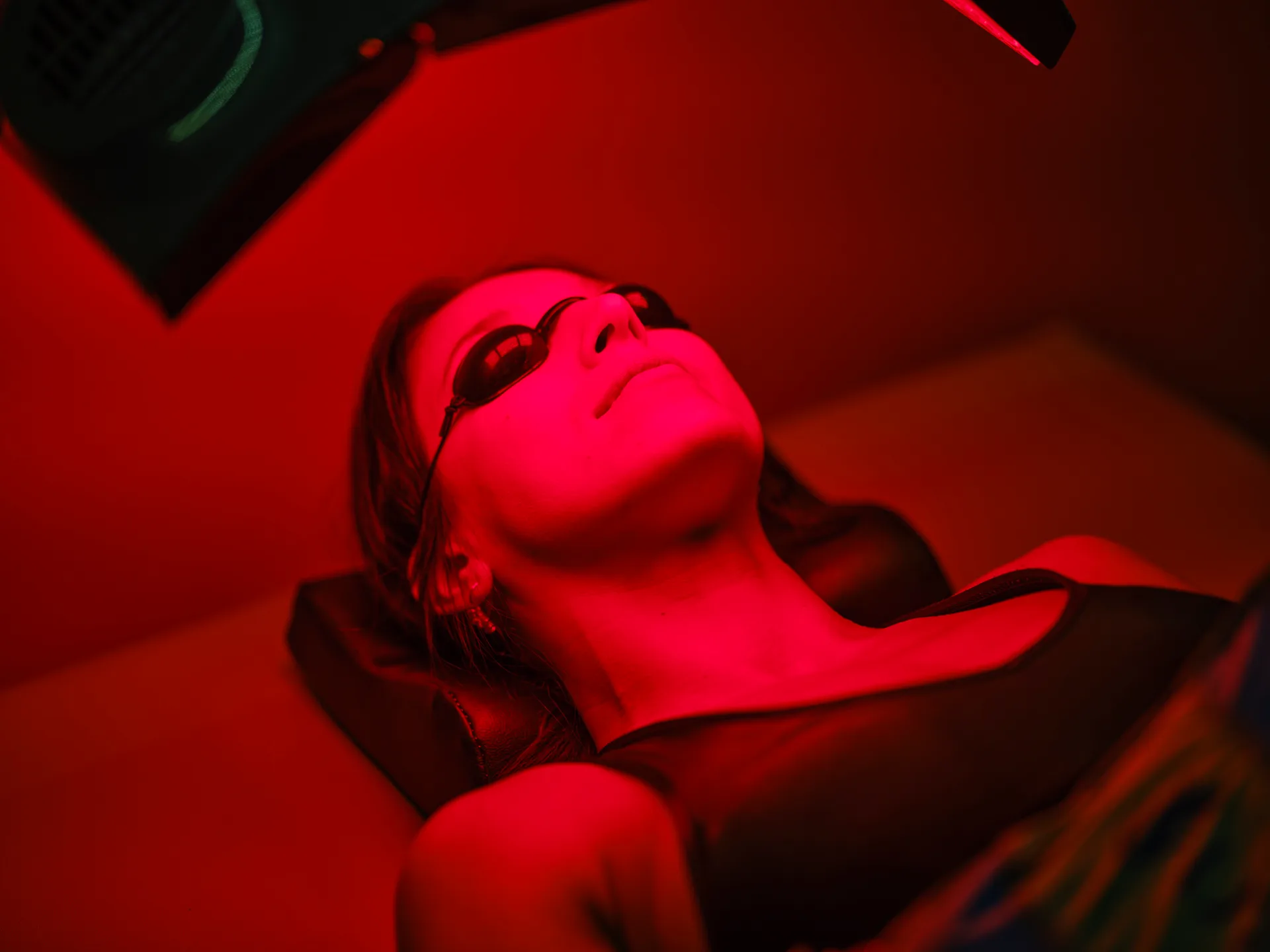 Woman wearing protective goggles lying under a red light therapy panel