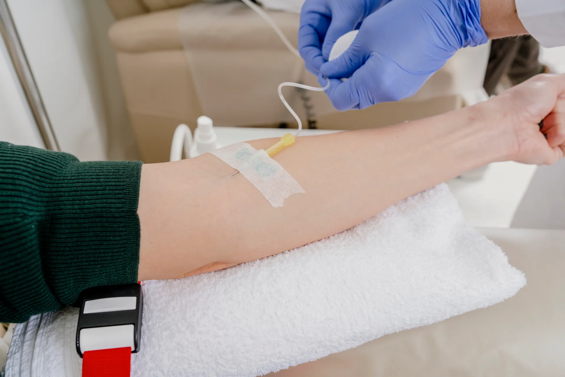 Gloved hand adjusting an IV line taped to a patient's arm resting on a towel