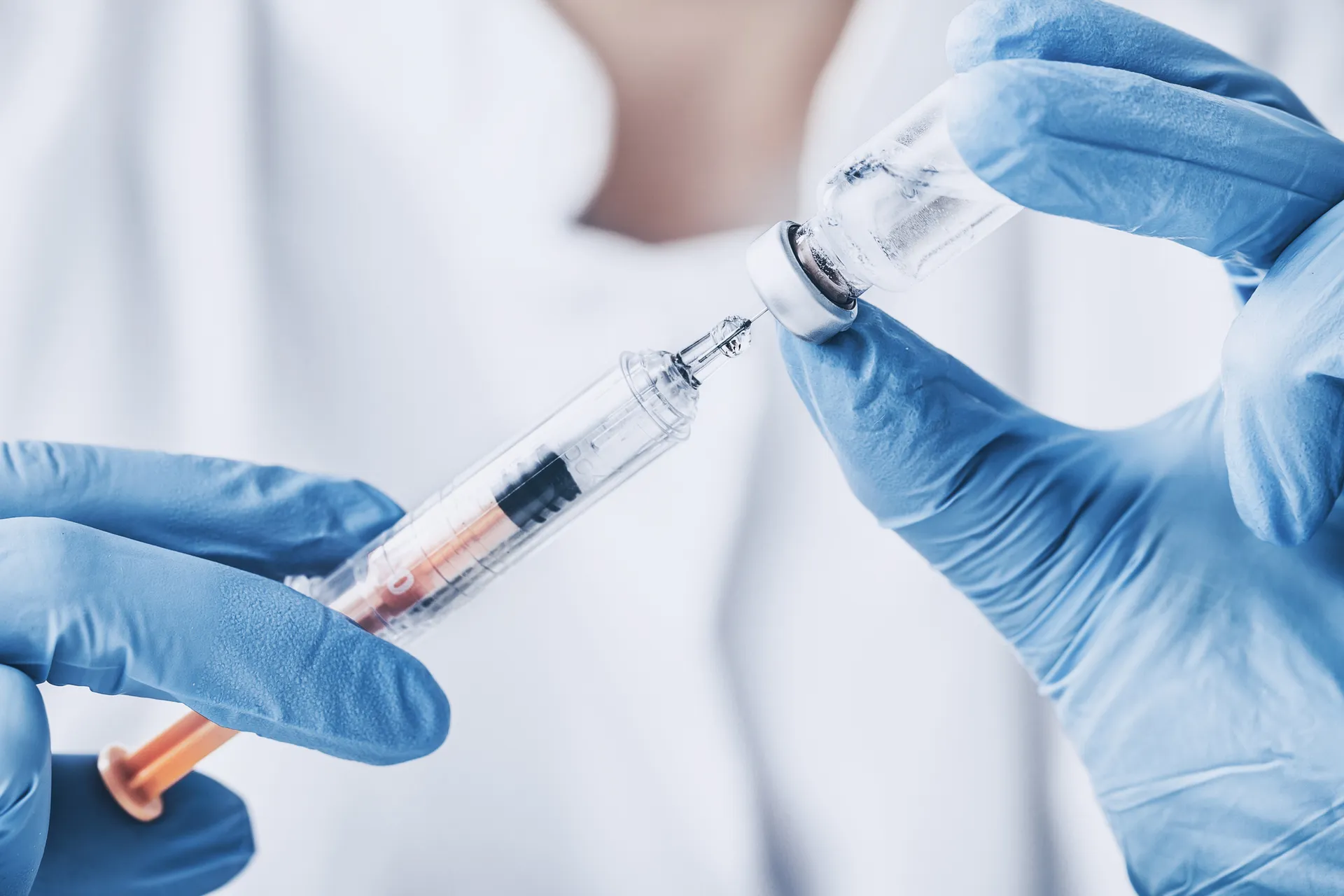 Gloved hands drawing liquid from a vial into a syringe
