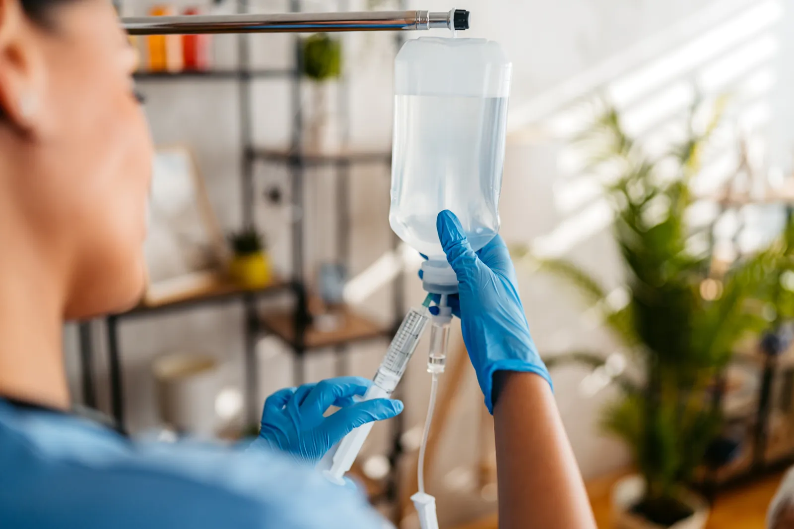 Clinician in blue gloves prepares an IV bag with a syringe