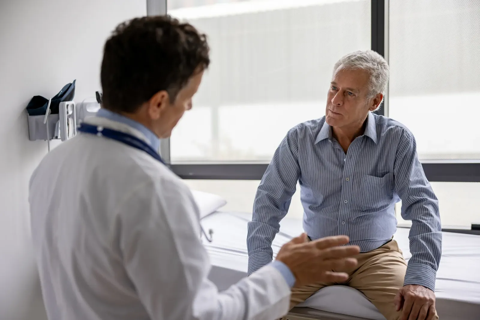 Doctor talks with an older man seated on an exam table in a bright clinic room