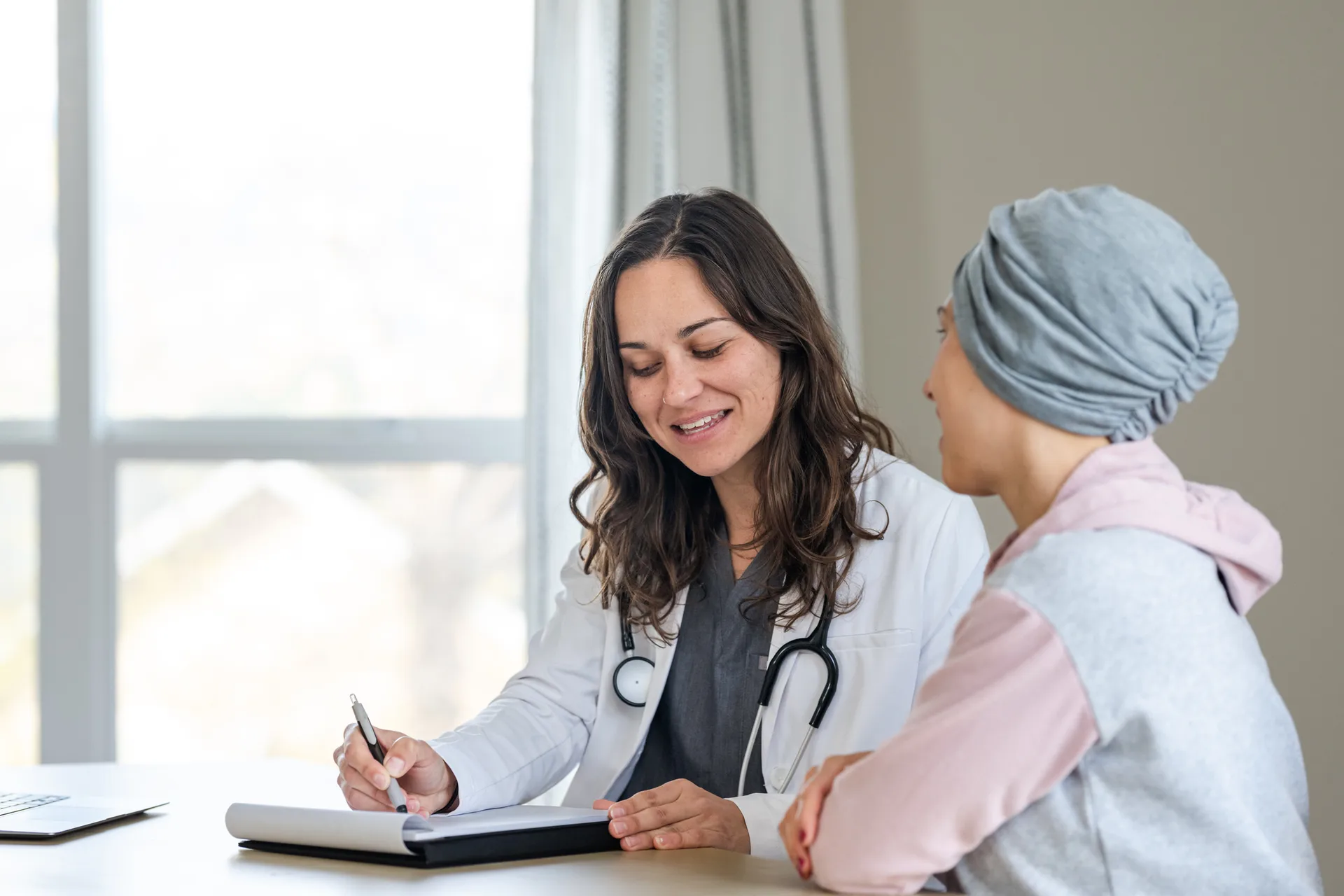 Smiling doctor taking notes while talking with a patient wearing a head wrap