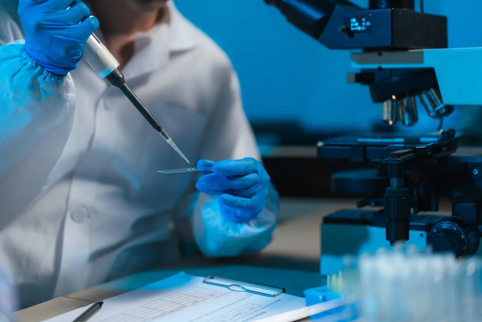 Lab scientist pipetting a sample onto a glass slide next to a microscope