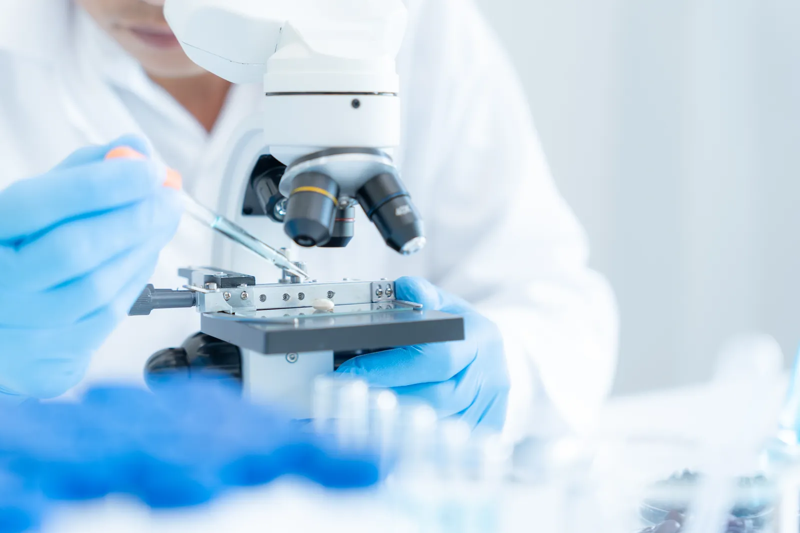 Lab worker in blue gloves places a sample on a microscope slide
