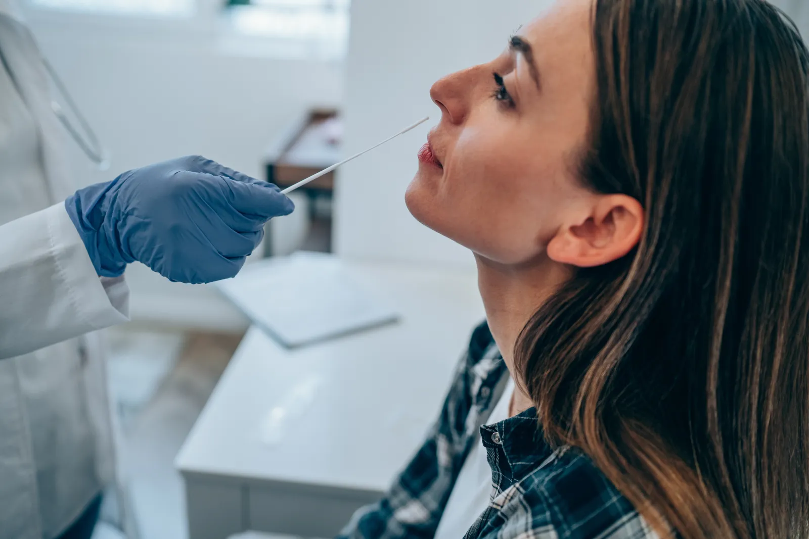 Gloved clinician inserts a swab into a woman's nostril