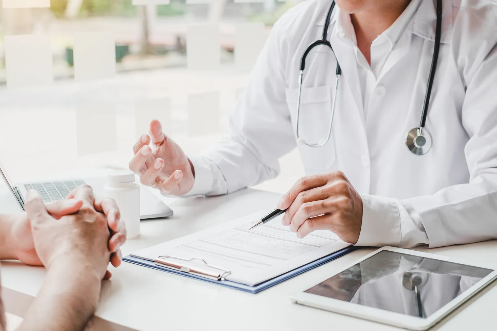 Doctor with a stethoscope explaining a document on a clipboard to a patient at a desk