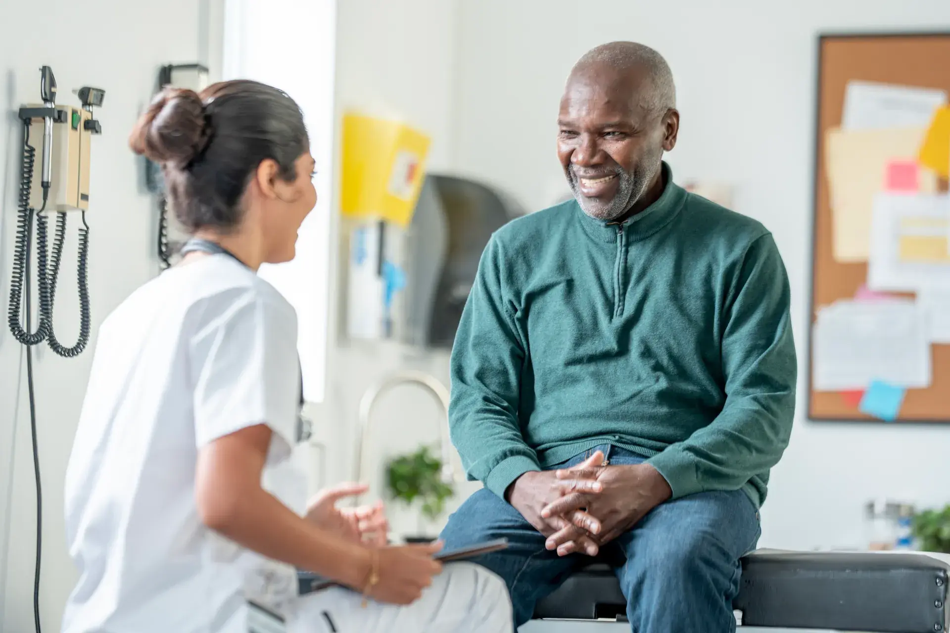 Smiling older man sitting on an exam table talking with a healthcare provider