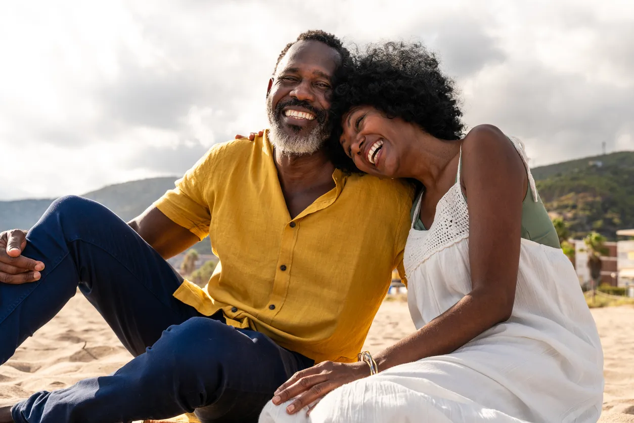 Laughing couple sitting close together on a sunny beach