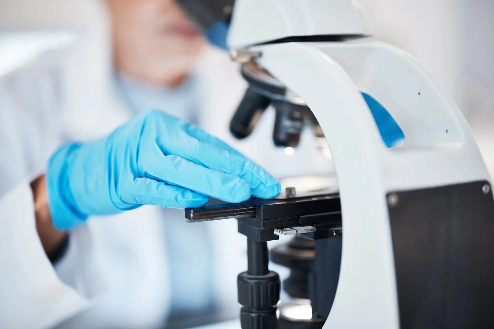Gloved hand placing a slide on a microscope stage in a laboratory