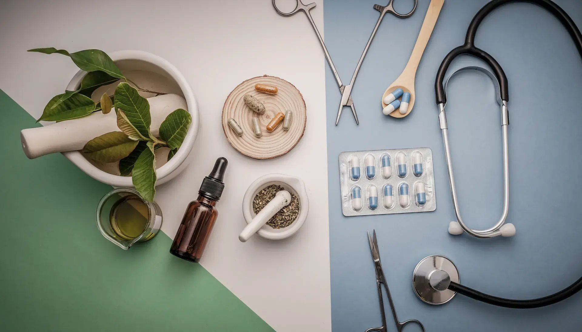 Herbs, mortar and pestle, dropper bottle and capsules beside pill packs, a stethoscope and medical tools