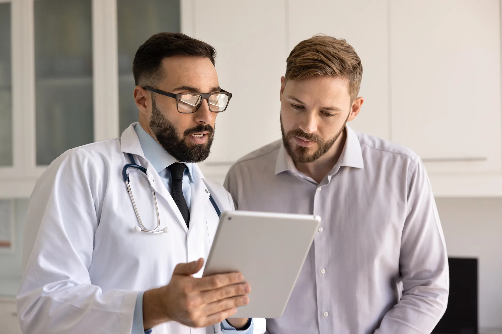 Doctor with a stethoscope reviews information on a tablet with a male patient