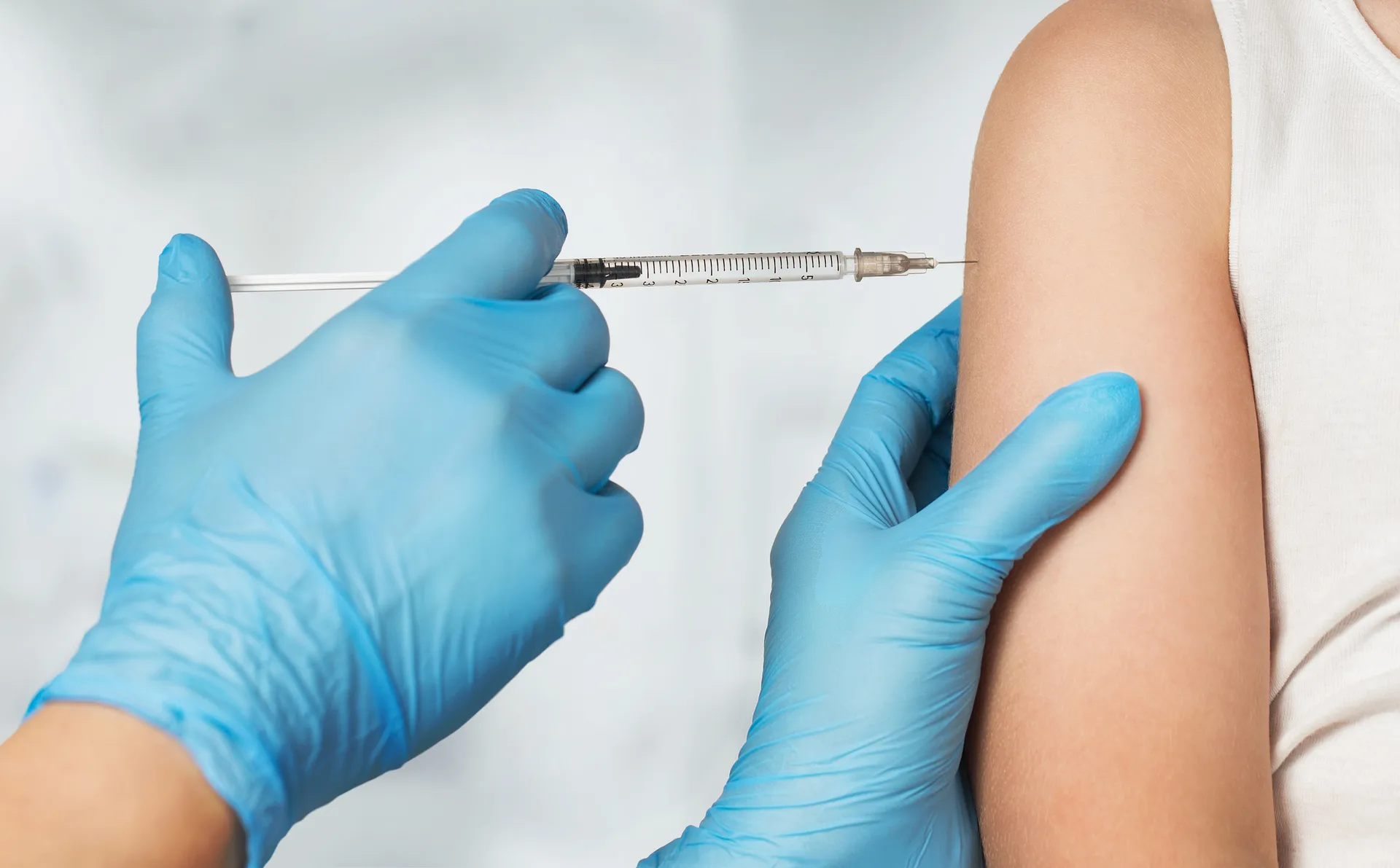 Gloved hands preparing to give an injection into a person's upper arm