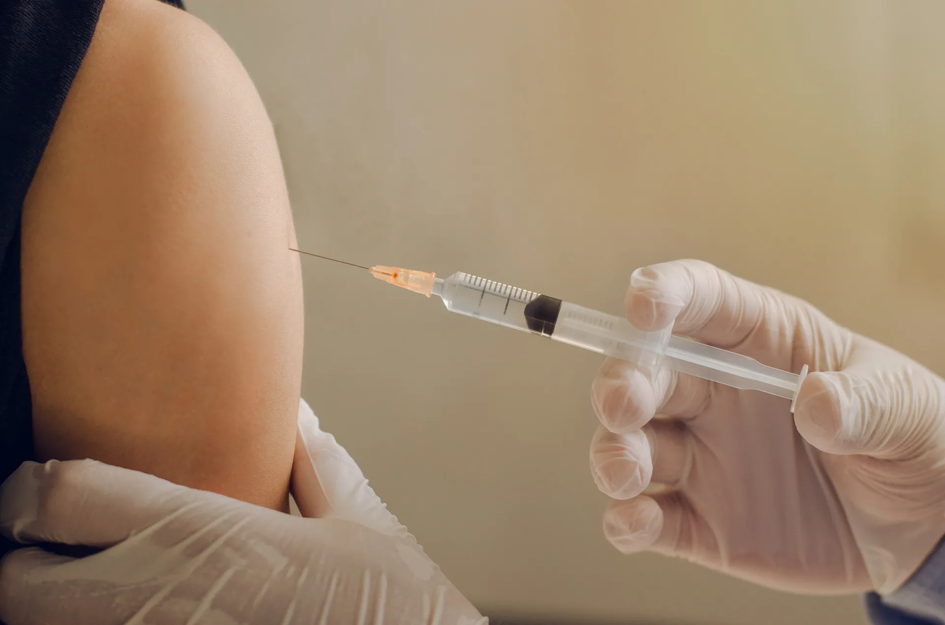 Gloved hand giving an injection into a person's upper arm