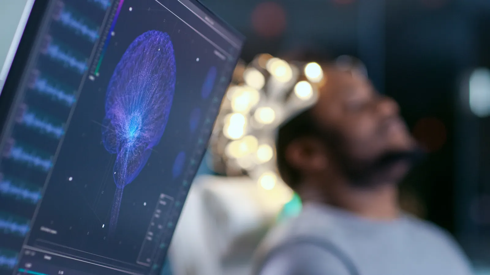 Man wearing a sensor headset with a brain activity visualization on a monitor in the foreground