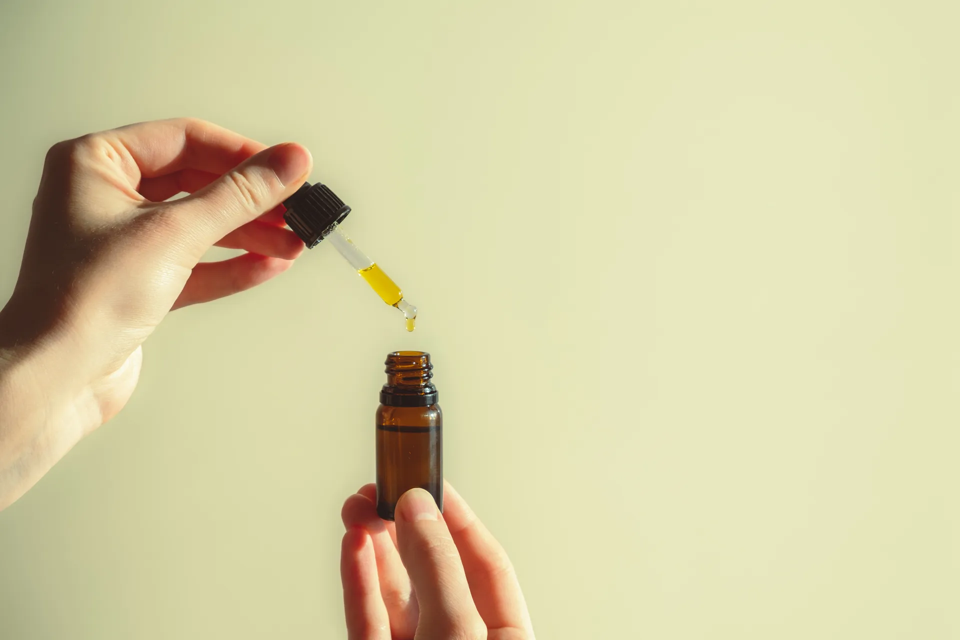Hands dispensing yellow drops from a dropper into a small amber bottle