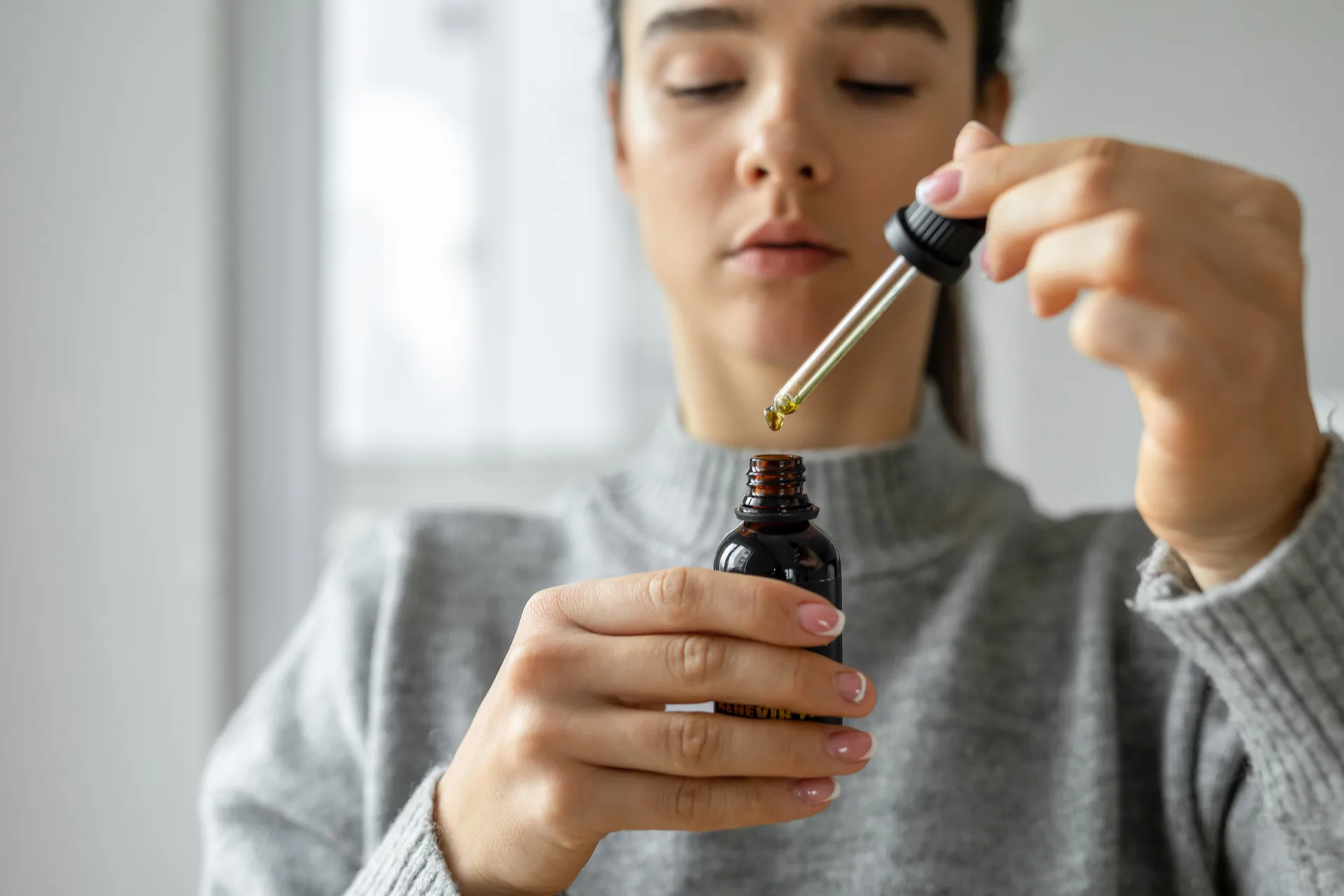 Woman holding a dropper over a small amber bottle
