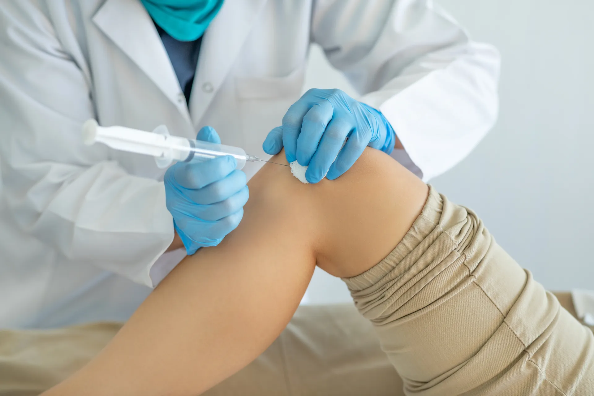 Gloved clinician injects a syringe into the side of a patient's knee