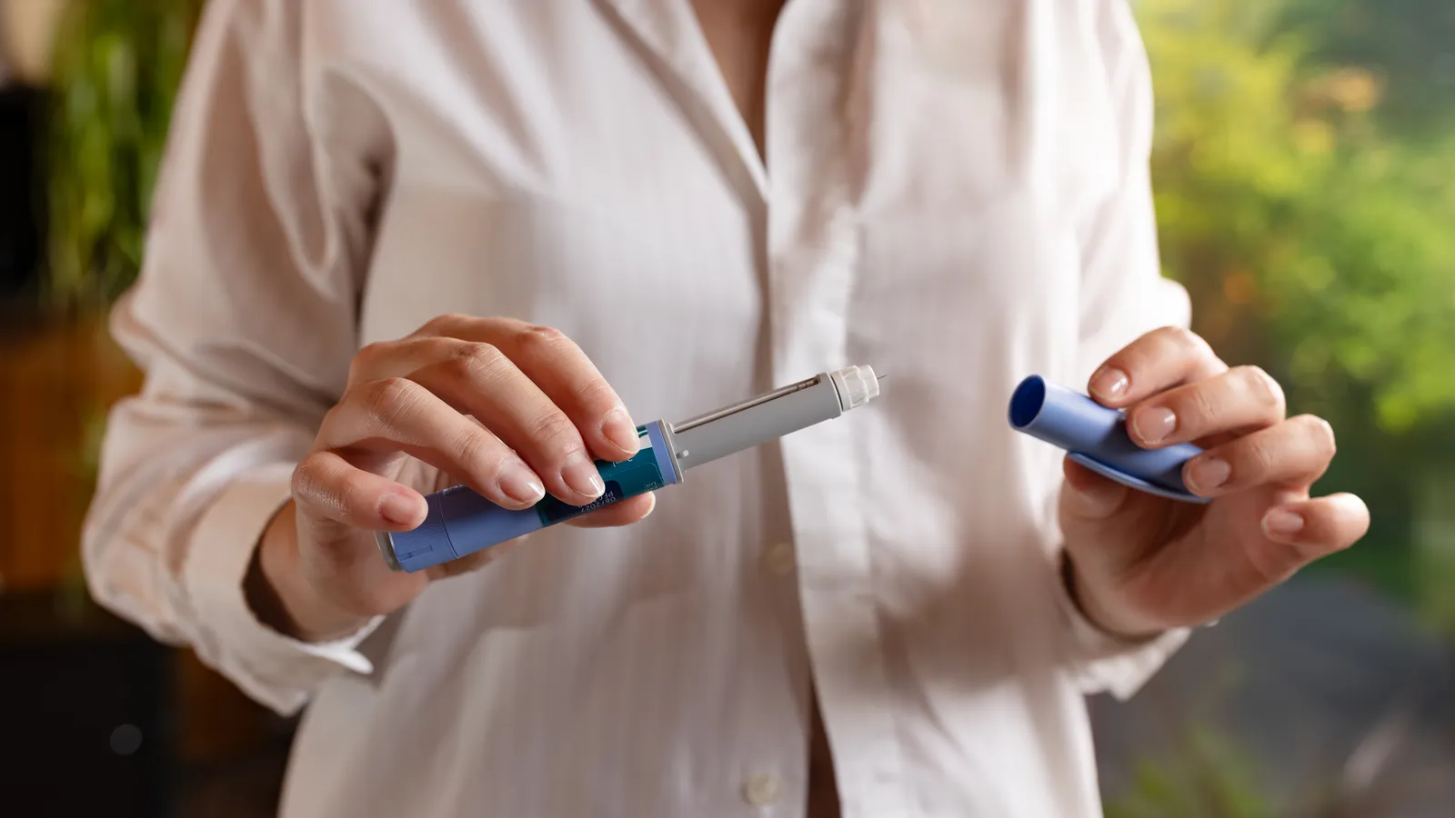 Woman in a white shirt holding an injection pen with its cap removed
