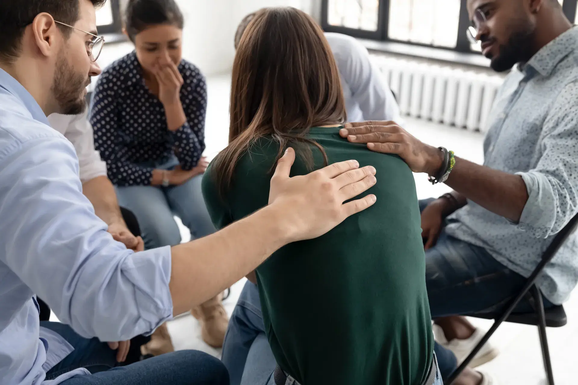 Group members comfort a woman by placing hands on her shoulders during a support session