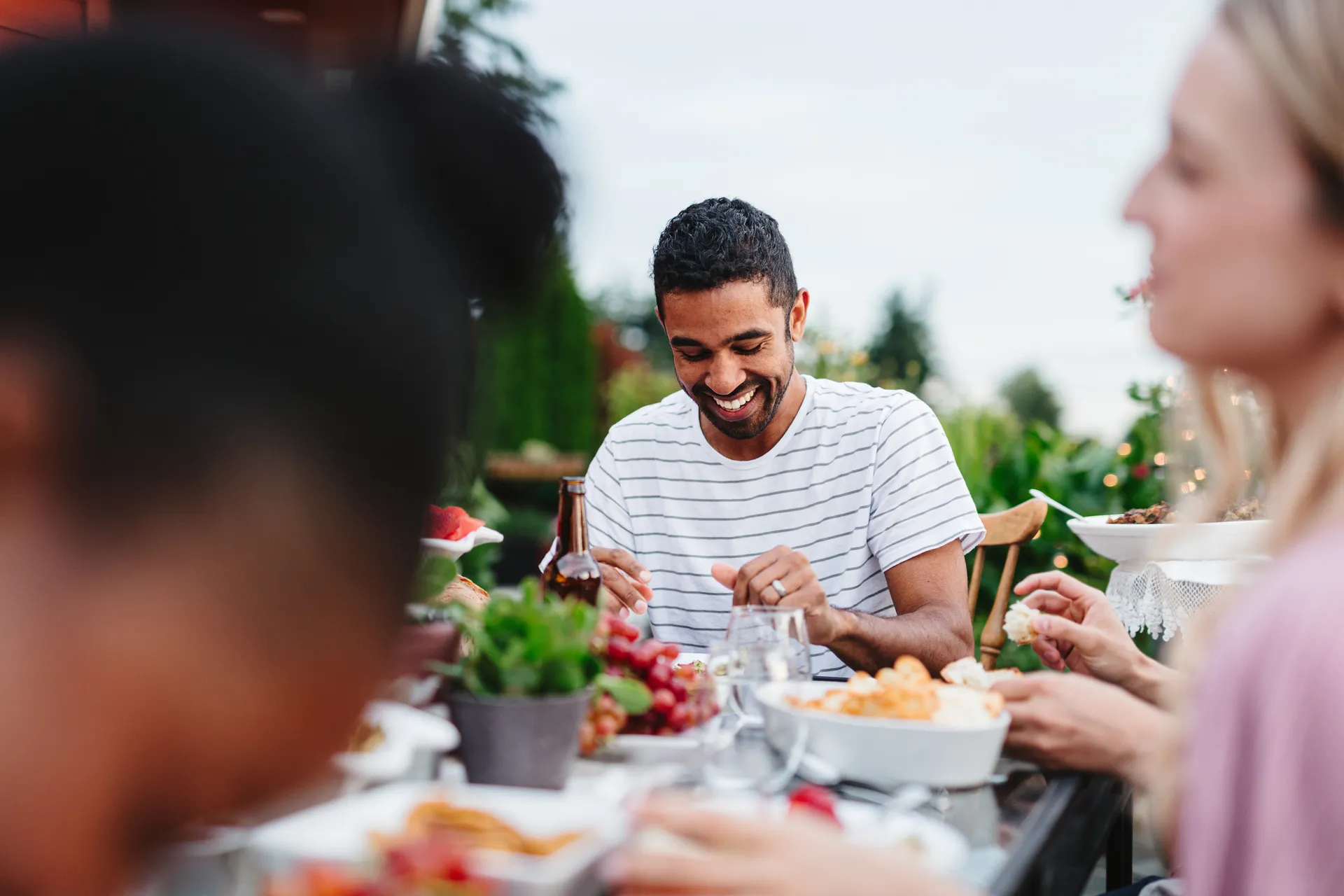 Smiling man enjoying an outdoor meal with friends at a garden table