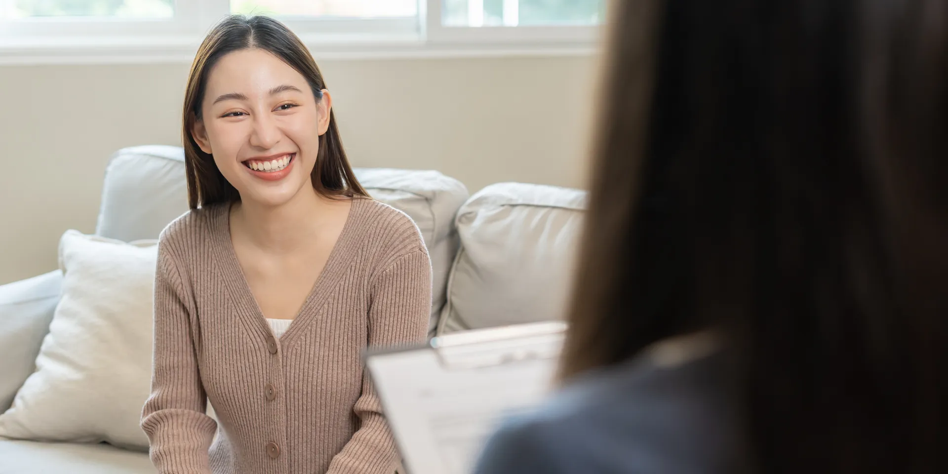 Young woman smiling on a couch during a counseling session with a practitioner holding a clipboard
