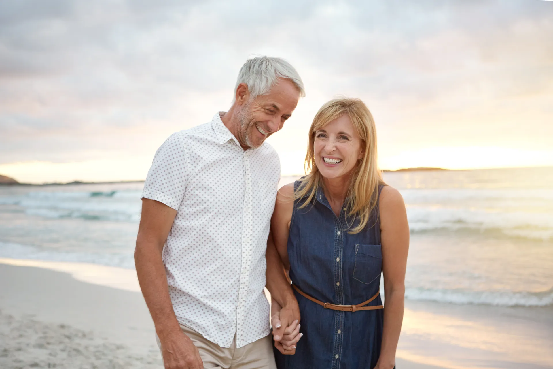 Smiling older couple holding hands while walking along the beach at sunset