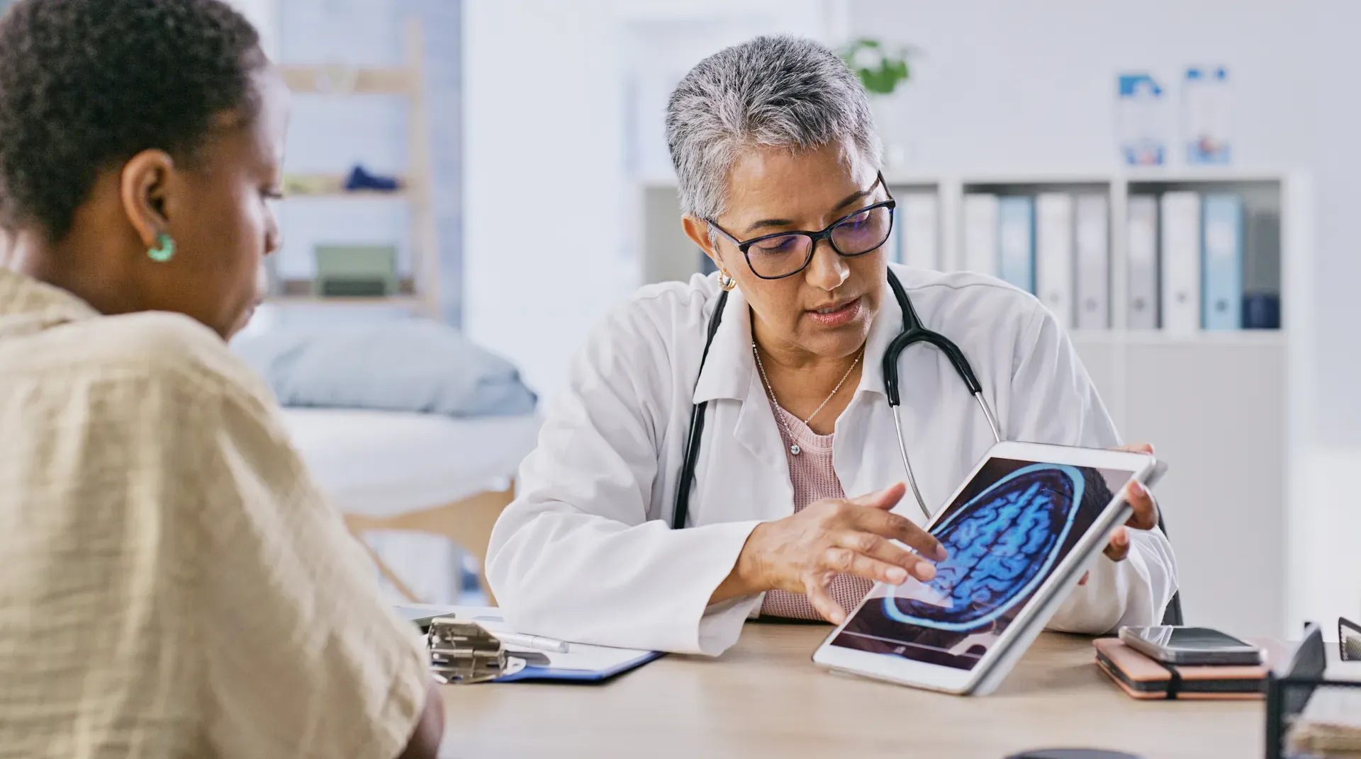 Doctor showing a patient a brain scan image on a tablet across a desk