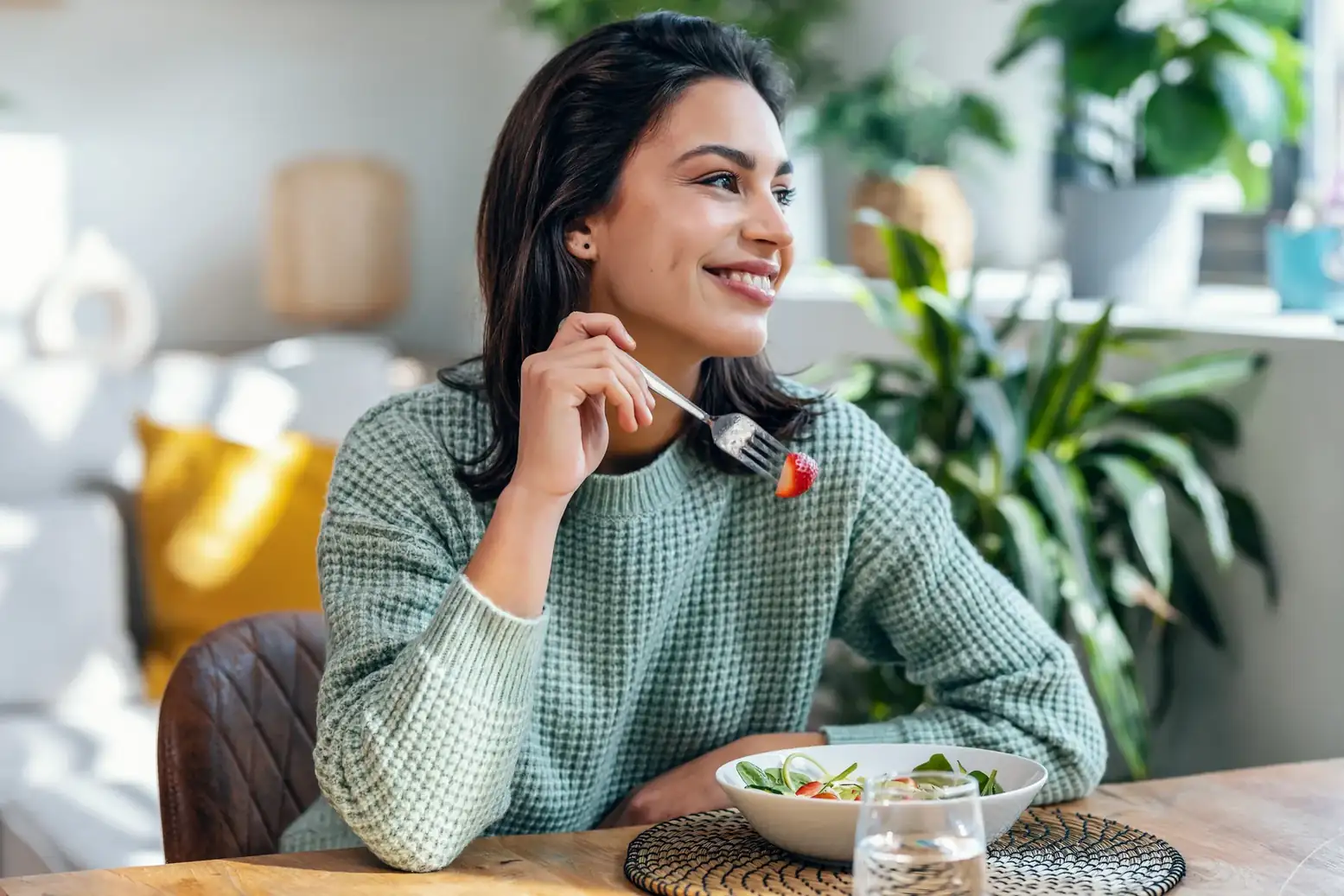 Smiling woman eating a salad at a table in a bright room