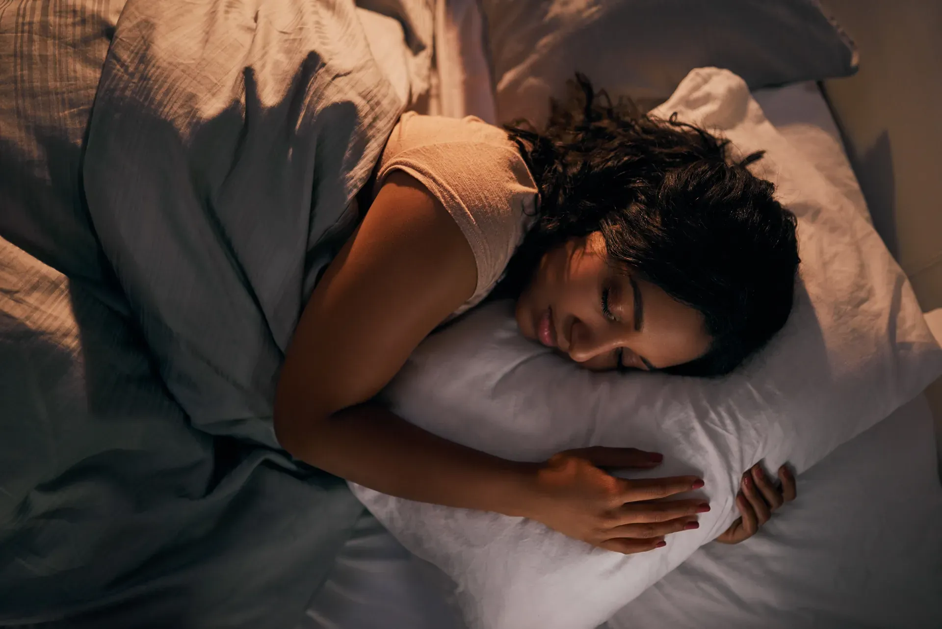 Woman sleeping peacefully in bed, hugging her pillow