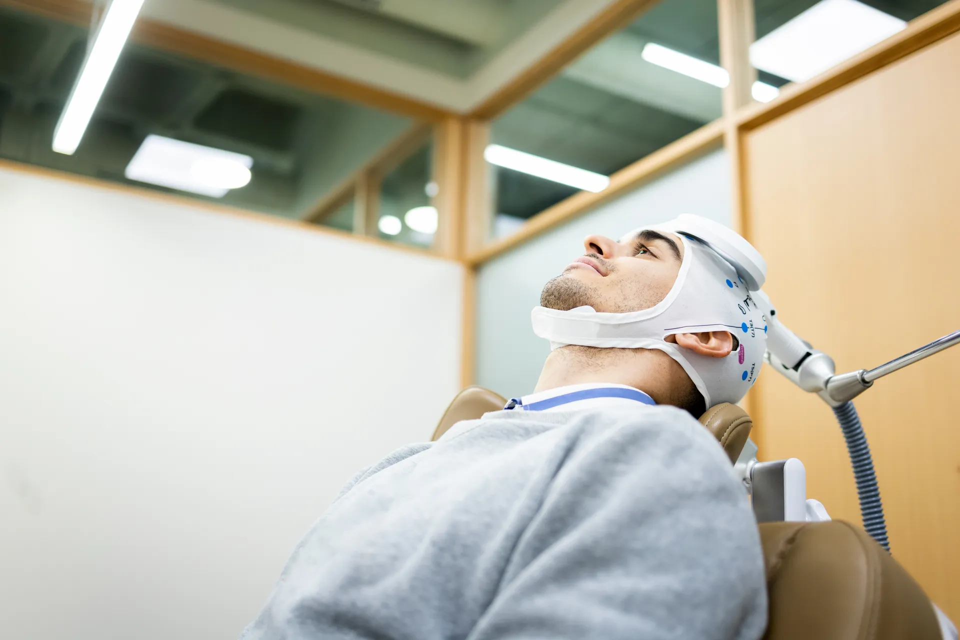 Man reclined in a treatment chair wearing a head cap with a magnetic stimulation coil