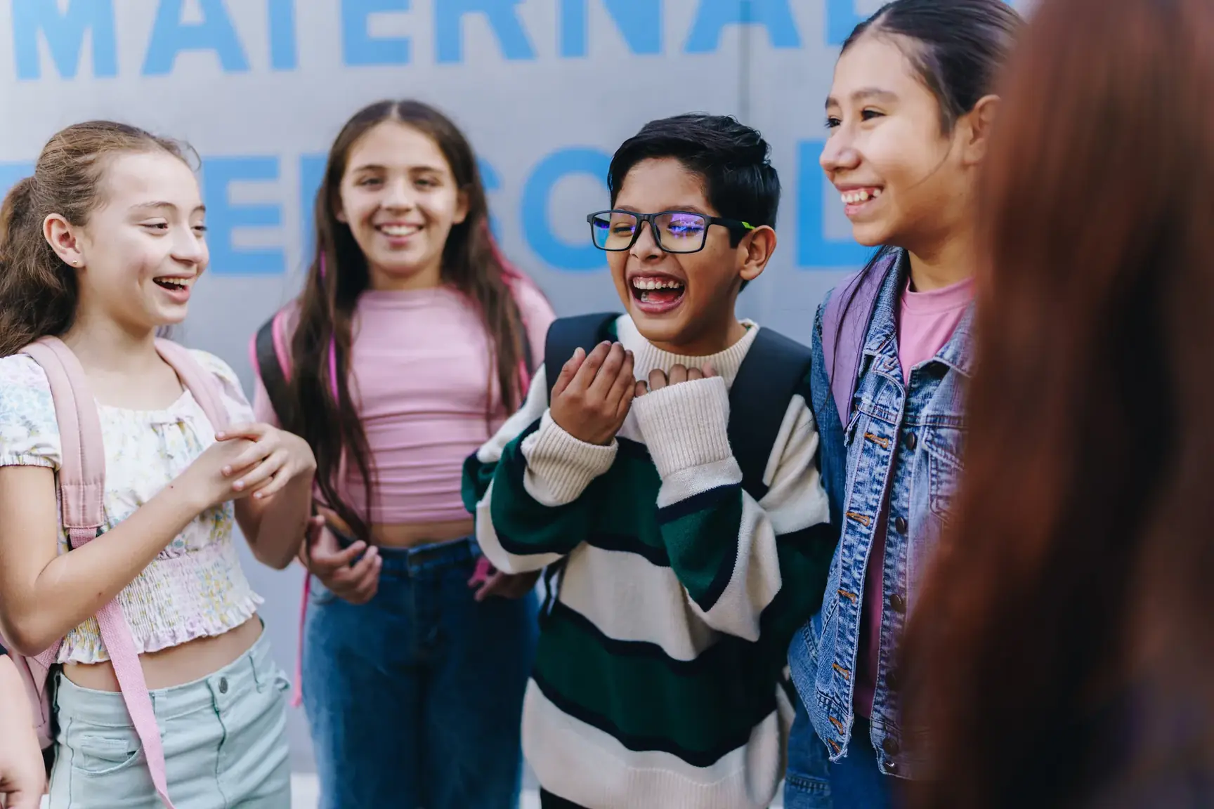 Group of laughing children with backpacks standing together outside a school