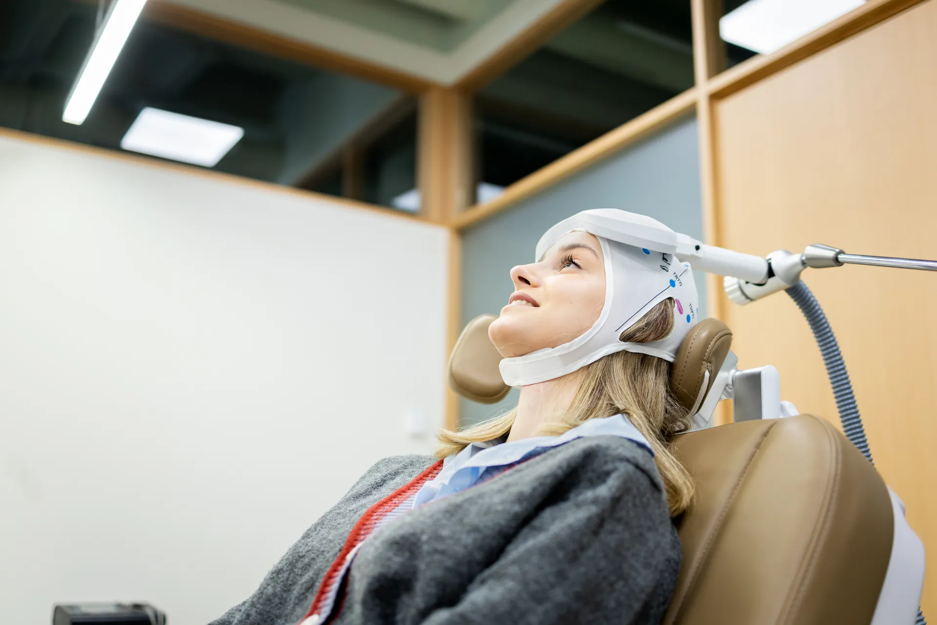 Woman reclining in a treatment chair wearing a head cap with a magnetic coil positioned against her head