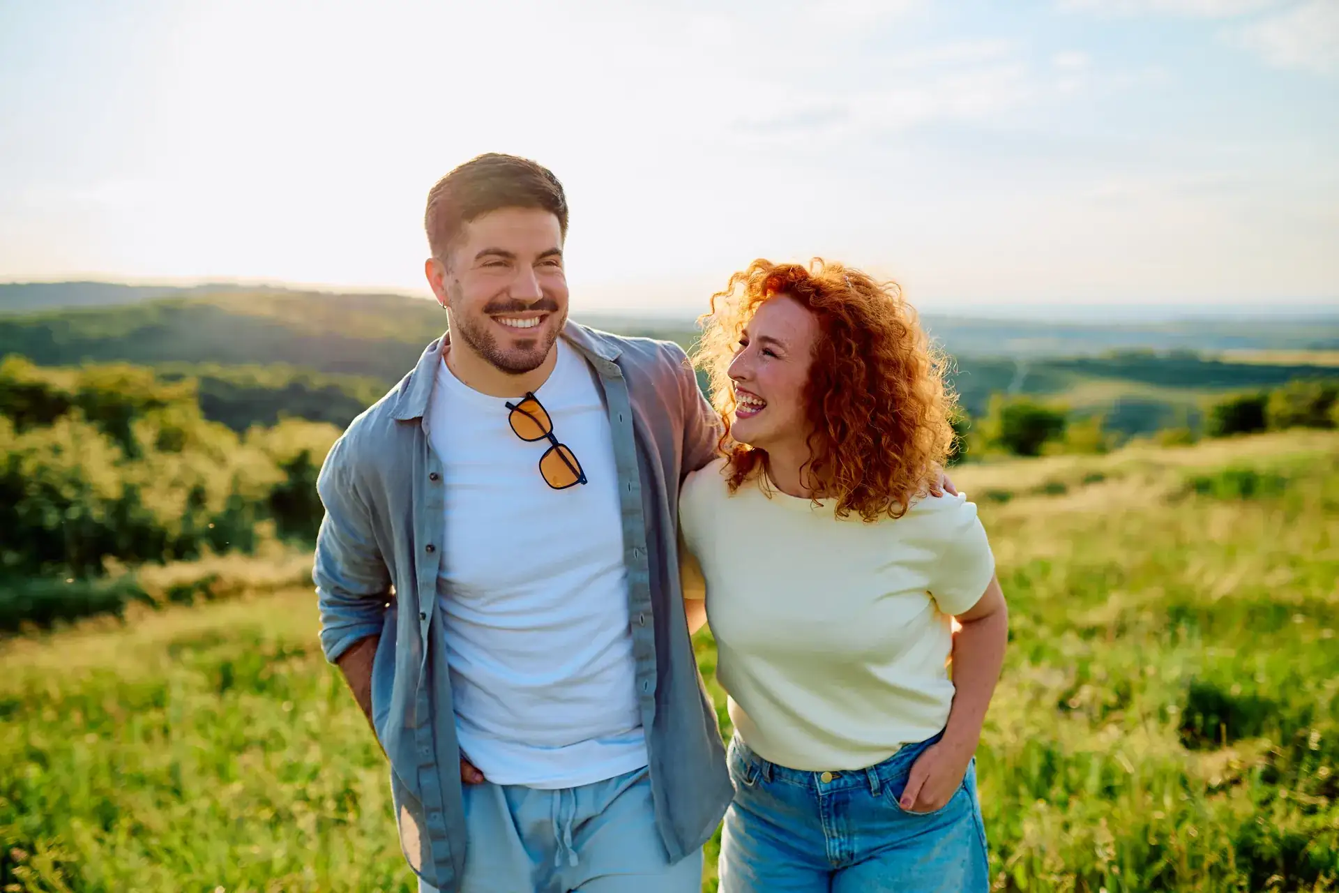 Smiling young couple walking together through a sunlit hillside meadow