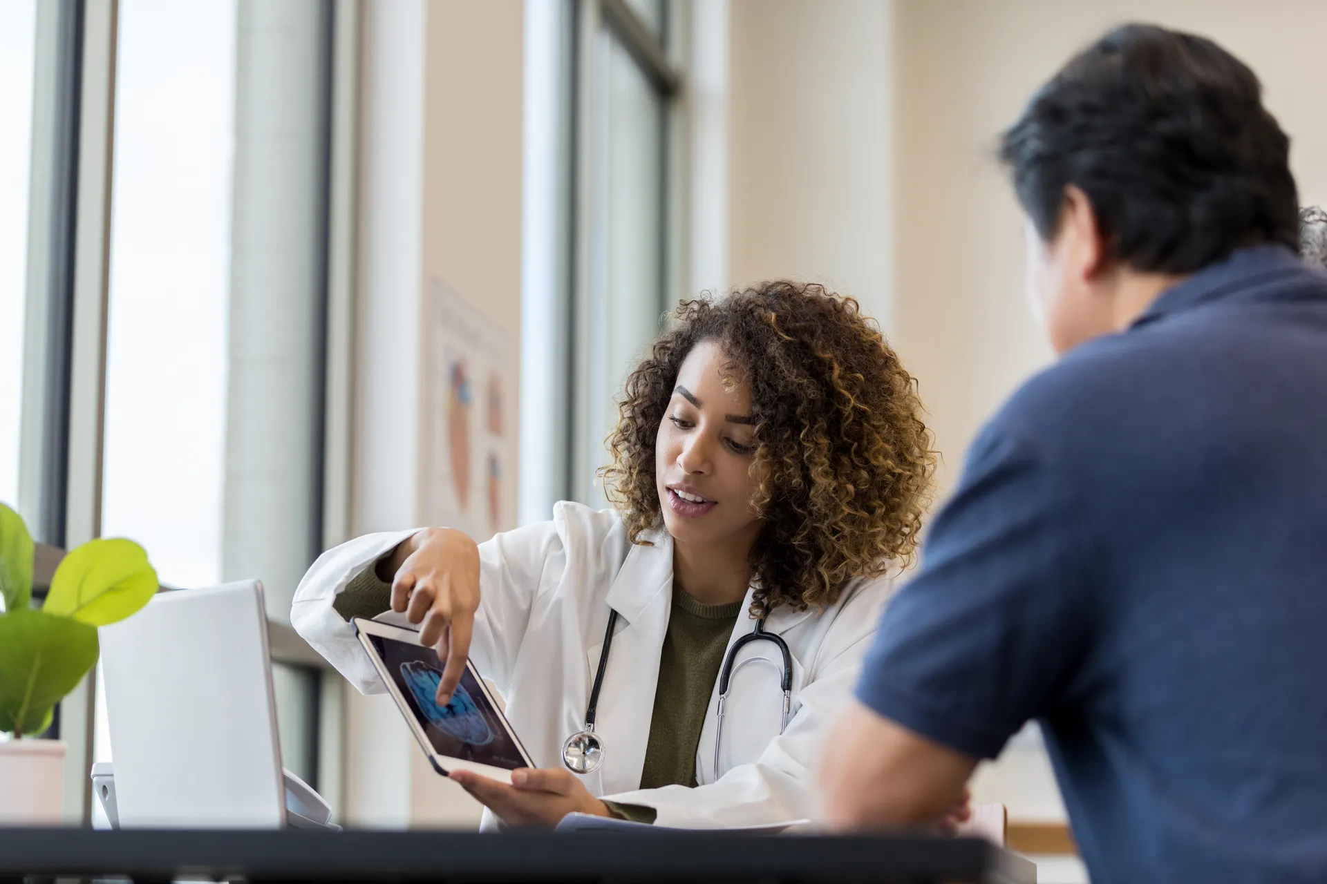 Doctor in a white coat showing a brain scan on a tablet to a male patient