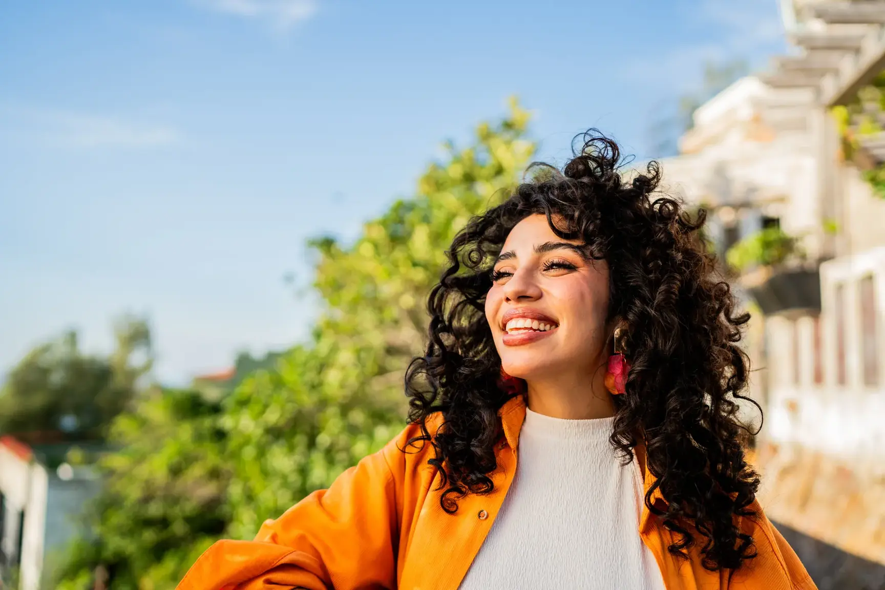 Smiling woman with curly hair and an orange jacket enjoying the sun outdoors