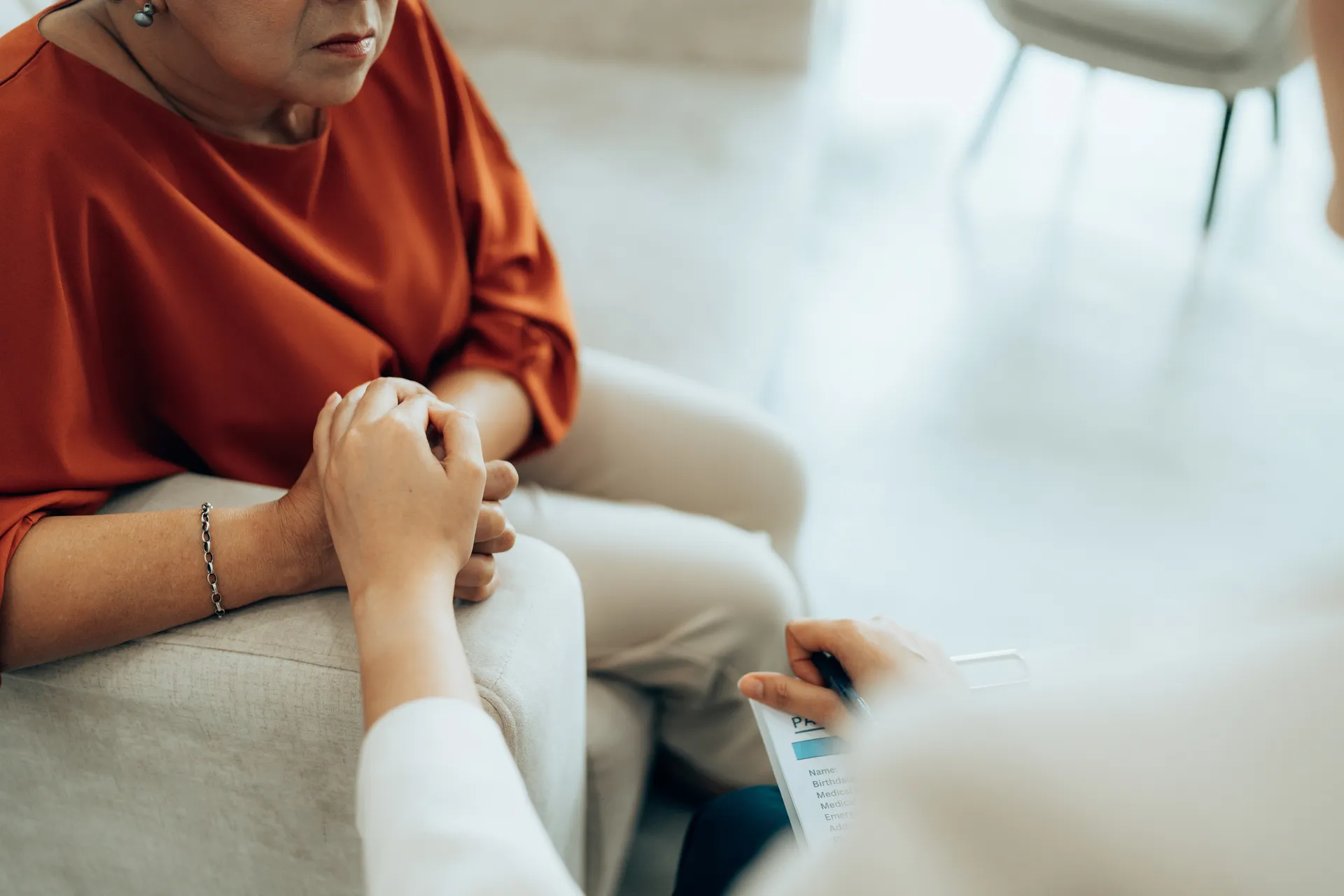 Clinician with a clipboard reaching out to comfort a seated older woman