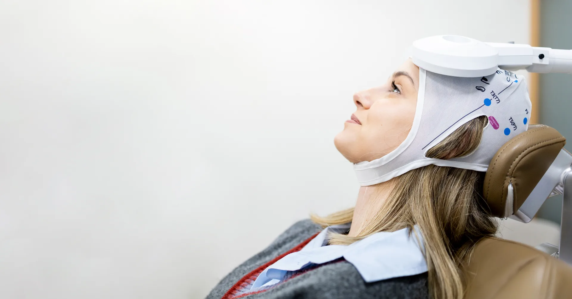Woman reclines in a treatment chair wearing a fitted cap with a TMS coil positioned against her head