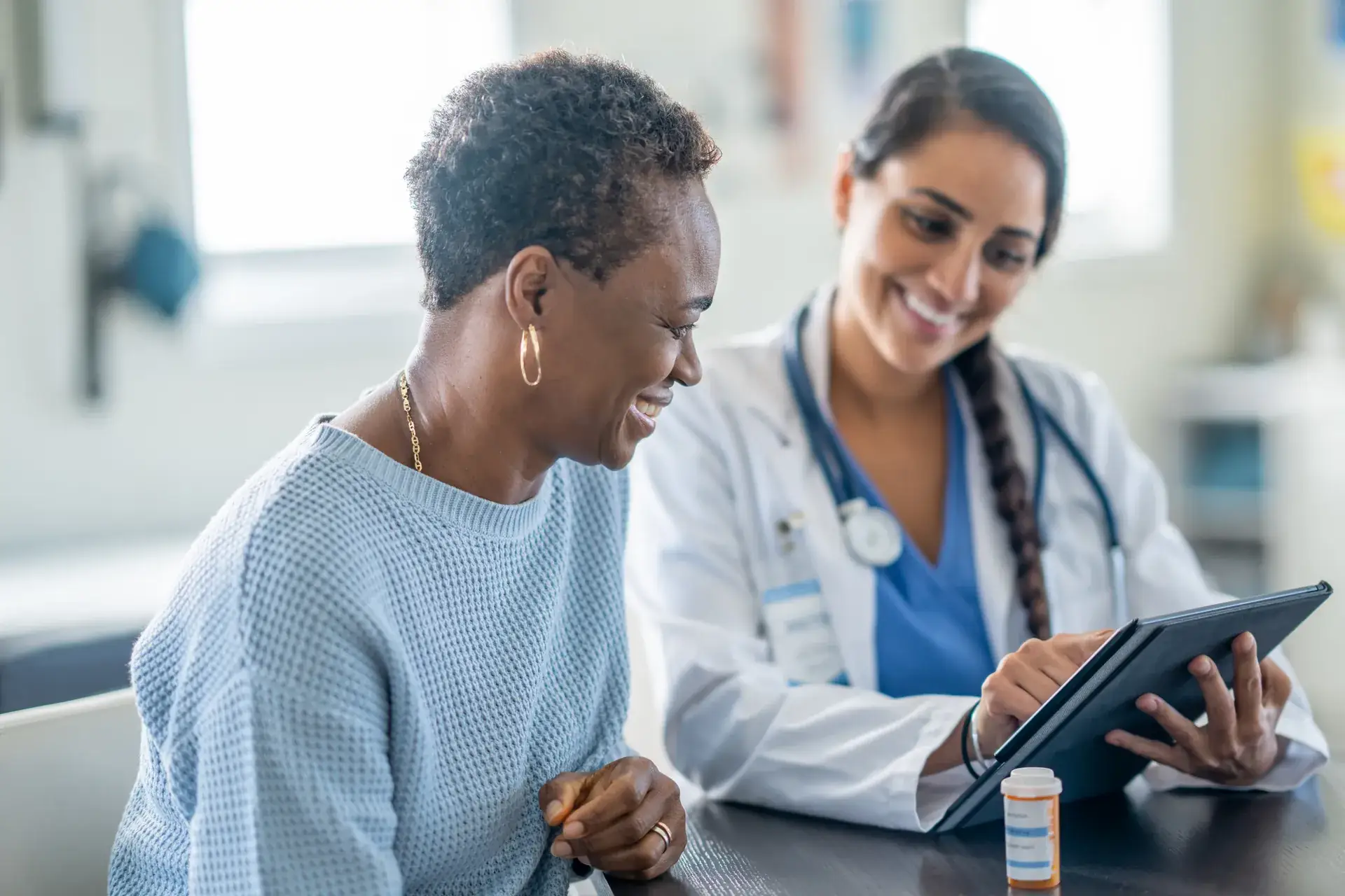 Doctor showing a tablet to a smiling patient beside a prescription bottle