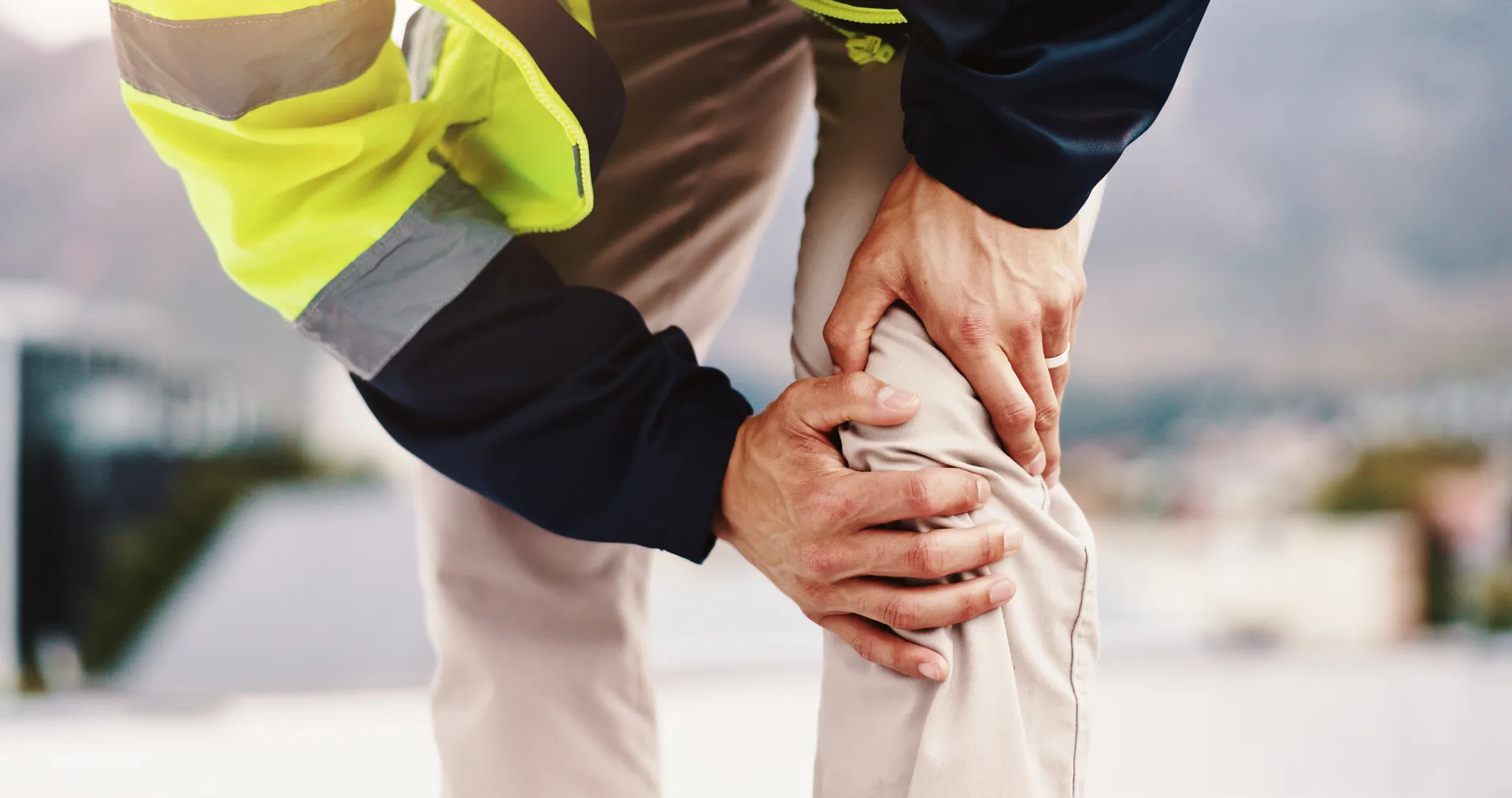 Person in a work jacket holds their knee in pain