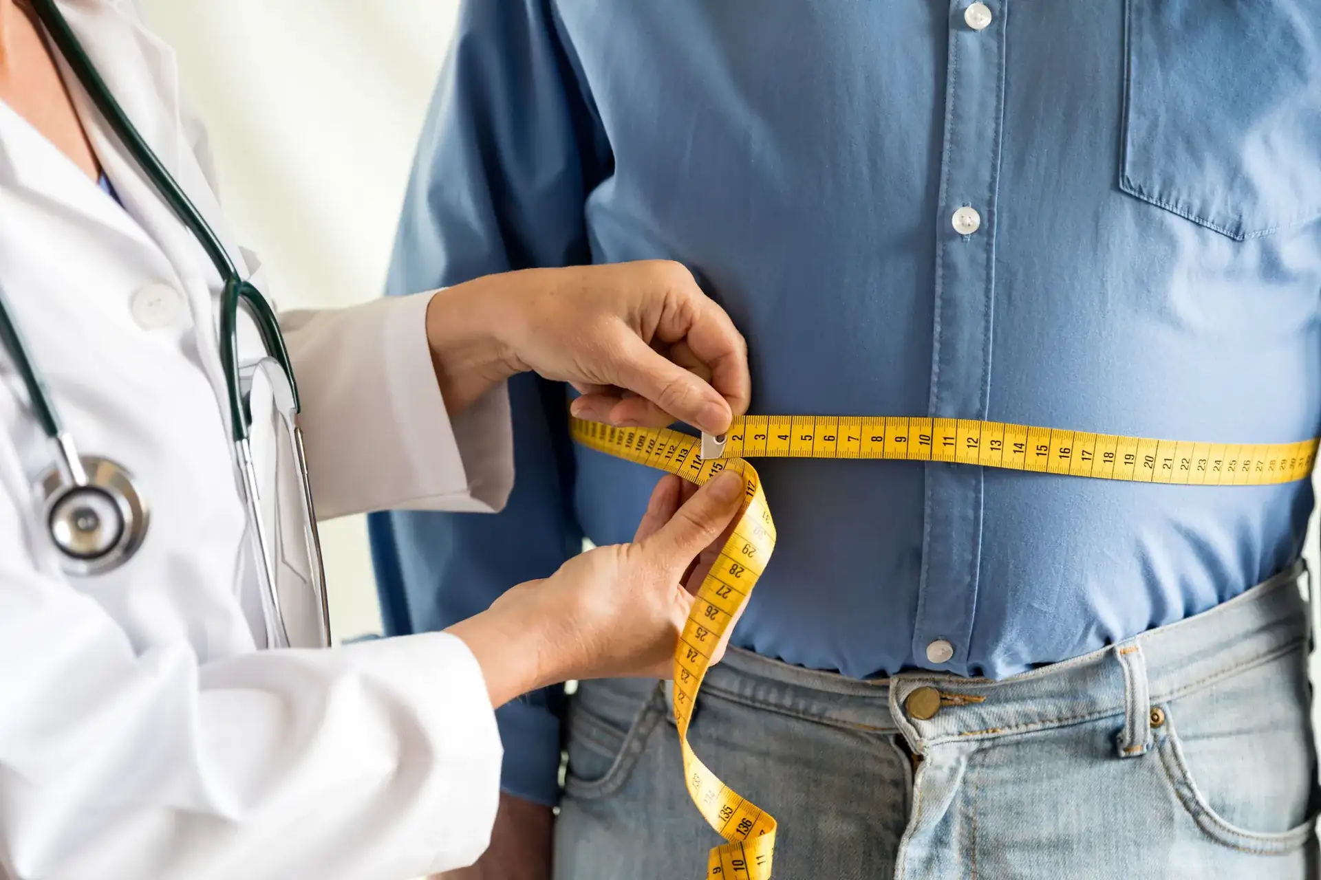 Doctor measuring a man's waist with a yellow tape measure