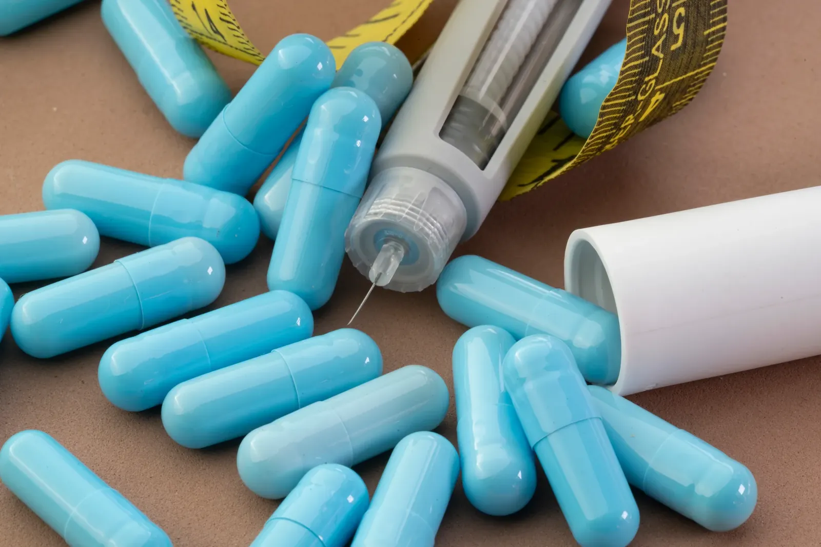 Blue capsules scattered around an injection pen and a yellow measuring tape