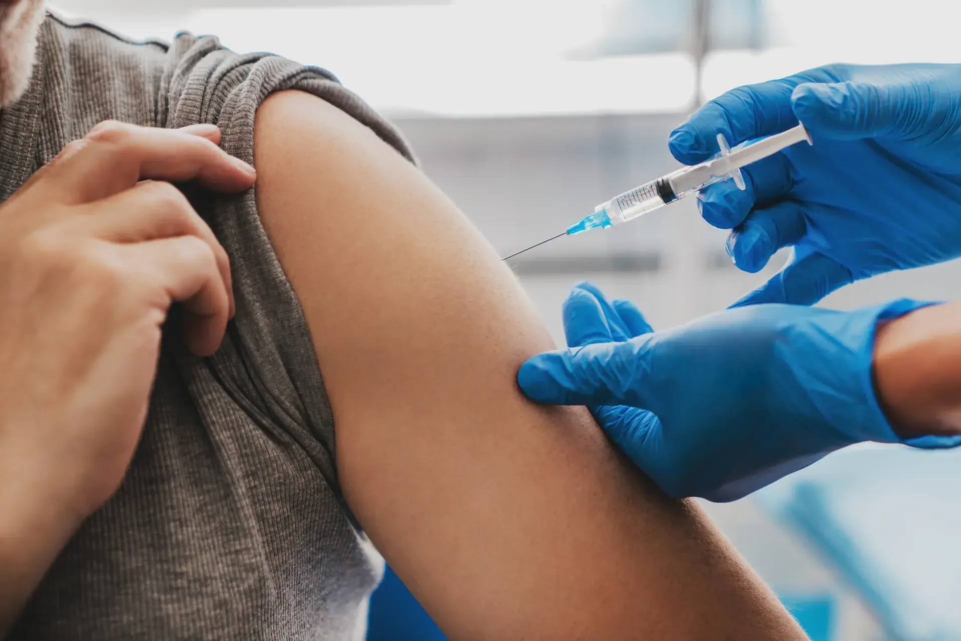 Gloved clinician giving an injection into a patient's upper arm