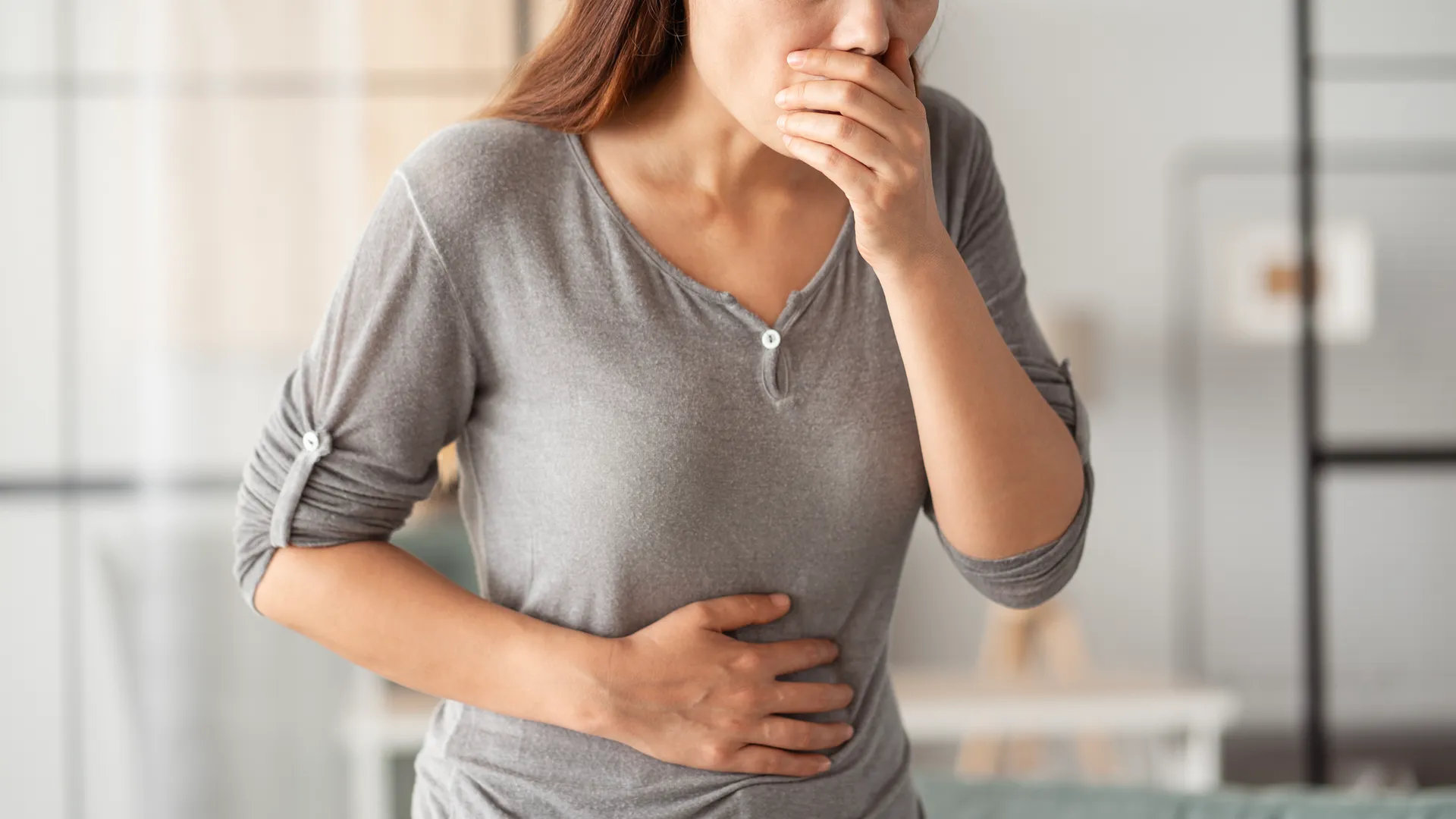 Woman covering her mouth with one hand and holding her stomach with the other, feeling nauseous